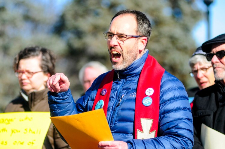 The Rev. Allen Ewing-Merrill speaks during a rally Wednesday in the plaza between the Burton M. Cross State Office Building and Maine State House in Augusta.