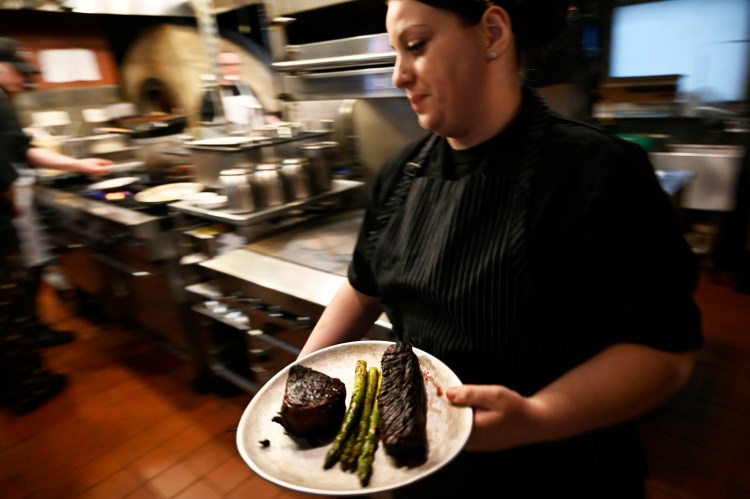 Kristen Cote, chef de cuisine at the Grill Room & Bar in Portland carries a plate of food in the kitchen.