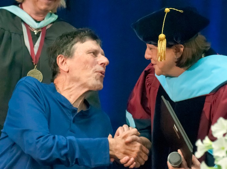 George Smith shakes hands with University of Maine at Augusta President Rebecca Wyke after receiving the Distinguished Achievement Award on Saturday during UMA's commencement ceremony at the Augusta Civic Center.