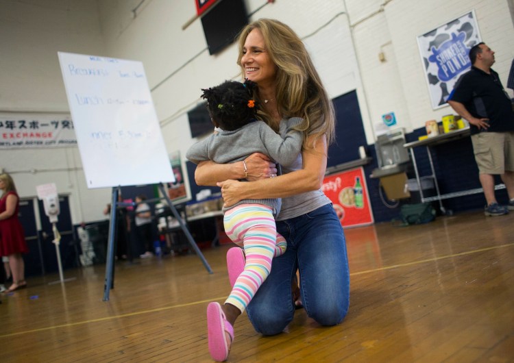 Volunteer Julie Haddad of Scarborough gives a hug to Melissa Paoula Ononye, 10, at the emergency shelter for asylum seekers at the Portland Expo.