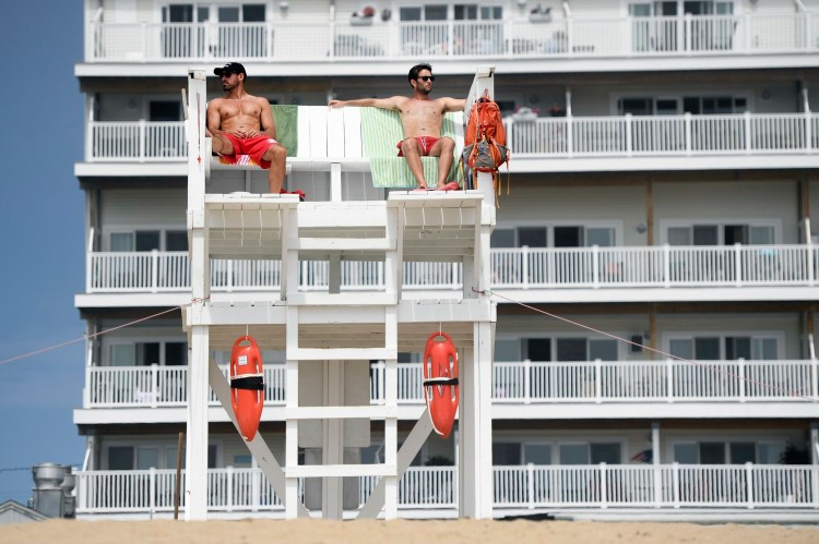 Assistant lifeguard captain Lance Timberlake, left, and lifeguard Bryce Lamontagne watch over the beach from the Brunswick tower in Old Orchard Beach on Friday. Timberlake, a high school teacher in Sanford, said, "It's a great job. ... You get to be on the beach all day."