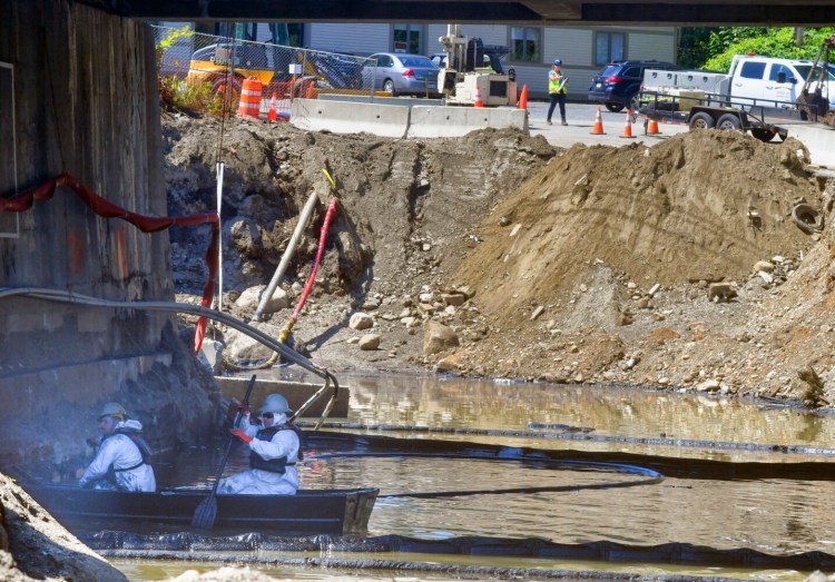 Workers paddle a boat through an oily lagoon under the Bridge Street bridge on Aug. 20 in Gardiner.