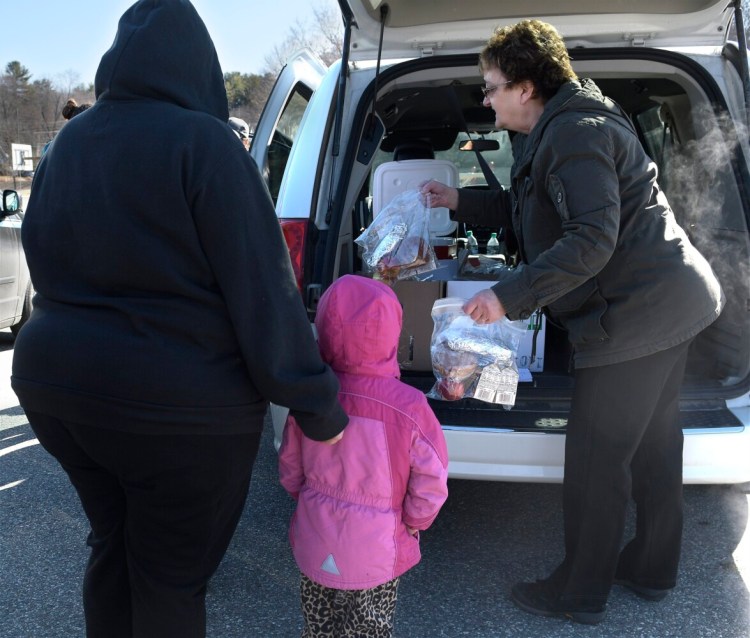 Augusta schools food service worker Sue Briggs serves bagged meals to children Monday morning at Williams Playground in Augusta. The food service department is preparing meals to students who aren't attending school, which has been canceled because of the coronavirus outbreak. 