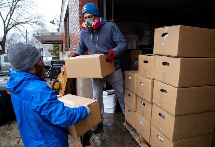 Nick DeSouza hands Portland Public Schools employee Nick McRae boxes filled with food  for families in need at Wayside Food Pantry on Friday. McRae loaded up his car with boxes and then drove them to Casco Bay Lines to be put out on to the ferry for island families. Portland Public Schools started doing a supplemental food drop for dozens of vulnerable families. The district reached out to Wayside Food Pantry to see if they could help. The food pantry usually does 60 to 80 food boxes a week and are now doing about 500 boxes a week. (Staff photo by Brianna Soukup/Staff Photographer)