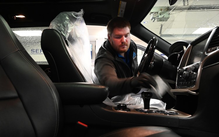 Sam Berry, a service advisor with Lee Auto Mall in Westbrook, cleans the interior of a vehicle after it was dropped off for service Monday. Car dealers in Maine are promoting repair and maintenance service while offering deals on car sales by phone or over the internet.