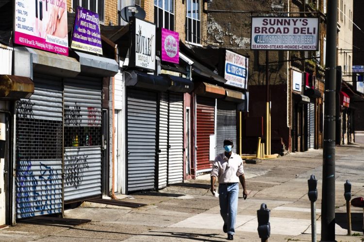 A person wearing a protective face mask as a precaution against the coronavirus walks past shuttered businesses Thursday in Philadelphia. Nearly 3.2 million laid-off workers applied for unemployment benefits last week as the business shutdowns caused by the viral outbreak deepened the worst U.S. economic catastrophe in decades.