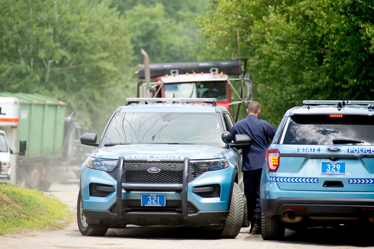 Maine State Police officers block access to the rear of the Narrow Gauge Distributors "Keeping the Supply High" building at 374 High St. in Farmington last Tuesday while marijuana plants are loaded into a shipping container, at left.