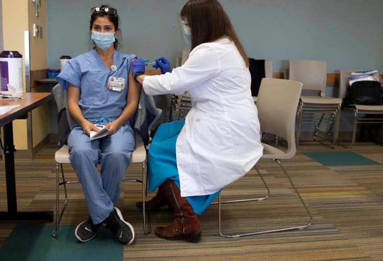 Kayla Mitchell, 31, a registered nurse who works in the Maine Medical Center's COVID-19 intensive care unit, receives the hospital's first dose from Dr. Christina DeMatteo on Dec. 15, 2020. 