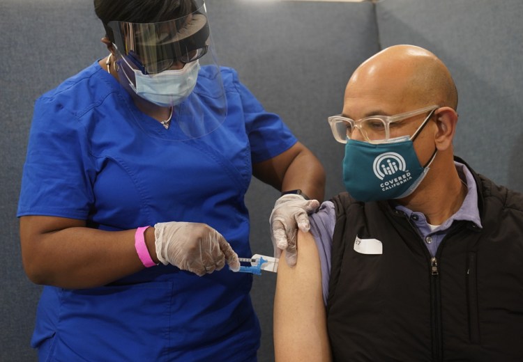 Licensed vocational nurse LeShay Brown inoculates California Health and Human Services Secretary Dr. Mark Ghaly at the Baldwin Hills Crenshaw Plaza in Los Angeles on Thursday. Public health experts say it's too early to say definitively why COVID-19 deaths are declining, but vaccinations are likely one factor.  