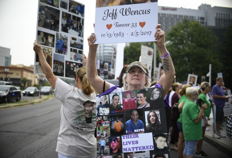 Lynn Wencus of Wrentham, Mass., holds a sign with a picture of her son Jeff and wears a sign of others' loved ones lost to OxyContin and other opioids during a protest Aug. 17, 2018, at Purdue Pharma LLP headquarters in Stamford, Conn.