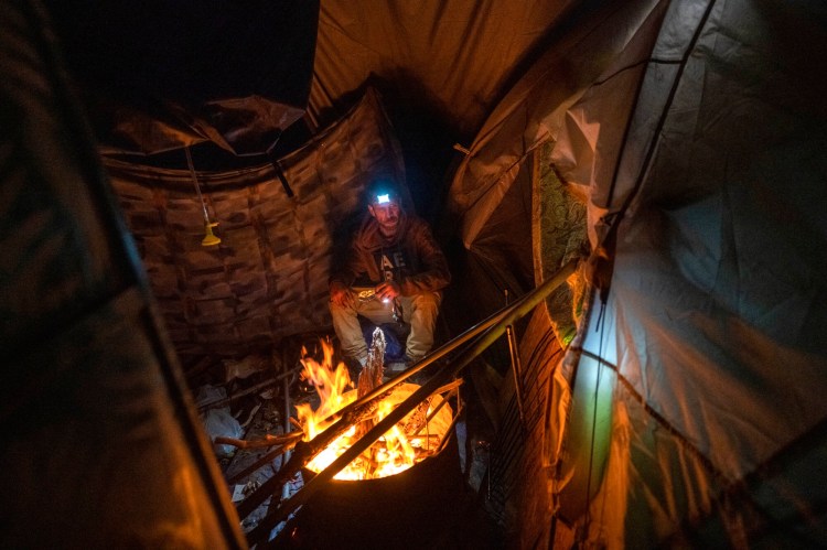 Shawn Stanford builds a fire Oct. 10 near the door to the tent he shared with his girlfriend, Amanda Frasier, at a homeless encampment in Waterville.