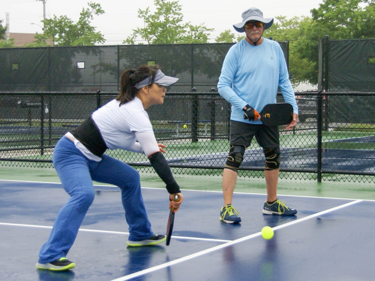 Rick Powell (right) watches his partner, Pan Zhang, return a low ball during a game at the MARC Pickleball Courts on Thursday, July 25, 2024.